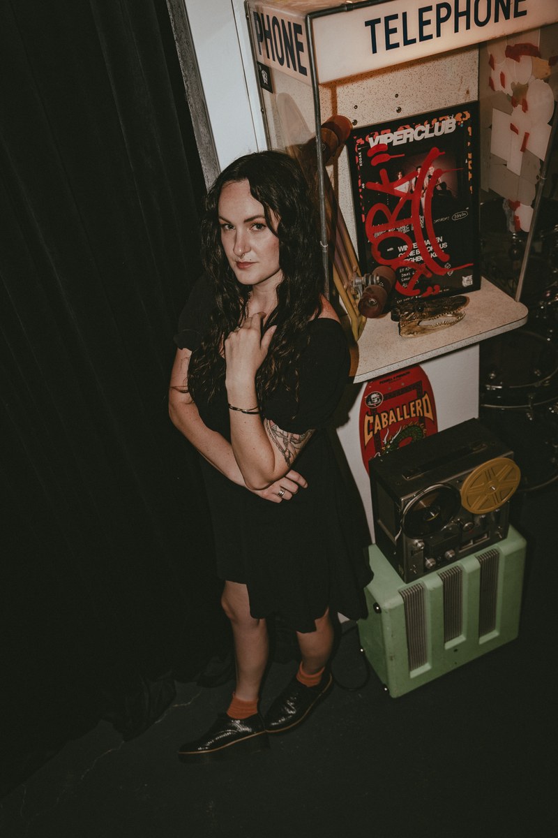 Brianna of Dork Social Club standing in the studio next to a vintage telephone booth and gear