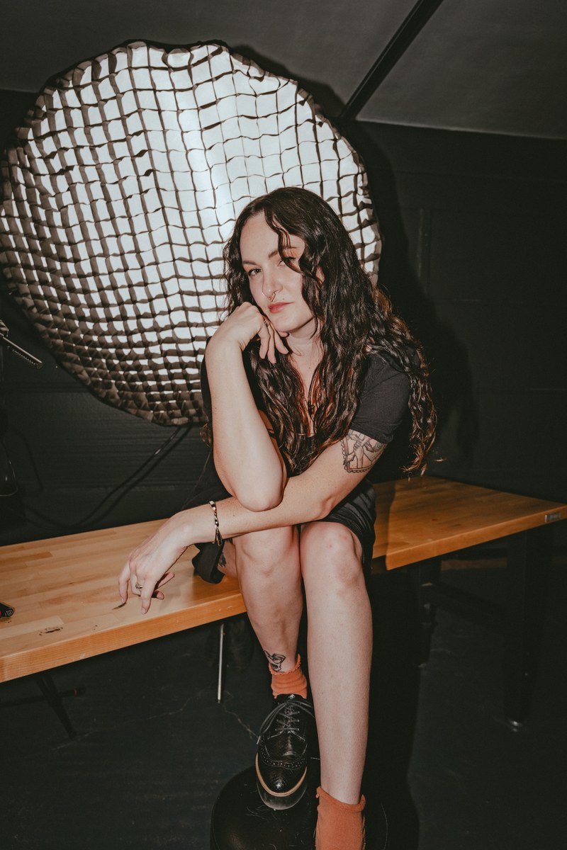 Brianna posing on a desk in front of a large softbox during a Dork Social Club studio shoot
