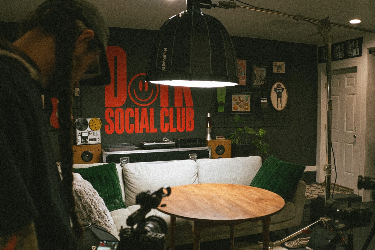 Behind the scenes of a Dork Social Club studio shoot with lights and cameras in front of the red logo wall